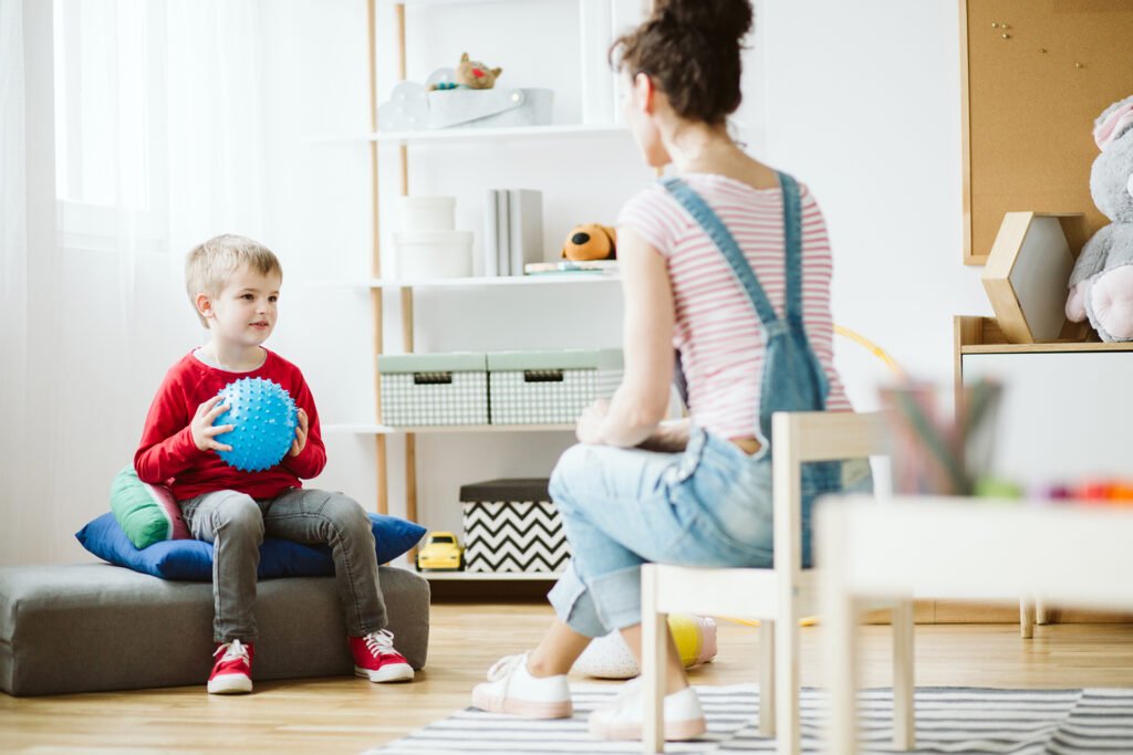 Cute little boy sitting on pouf and holding blue ball during ADHD therapy